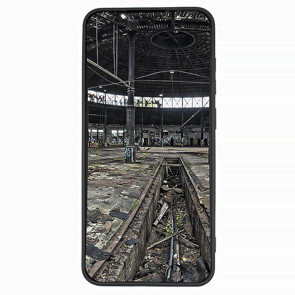 Ein Galaxy A37 – JT Berlin Pankow Soft Case umrahmt ein Smartphone, auf dessen Bildschirm ein verlassenes Lagerhaus mit Trümmern zu sehen ist – alles sichtbar durch den Bildschirm des Geräts und die stilvolle JT Berlin-Hülle.