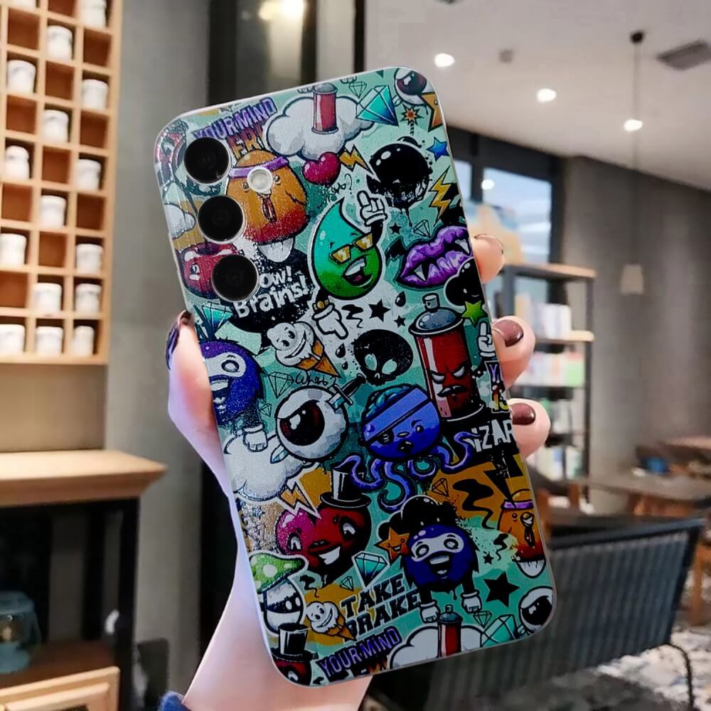 Eine Hand hält ein Galaxy A56 5G mit stilvollem Cover von Cover-Discount: Cartoon-Doodle-Motiv und transparentem Rand, perfekt für Trendsetter im modernen Café.
