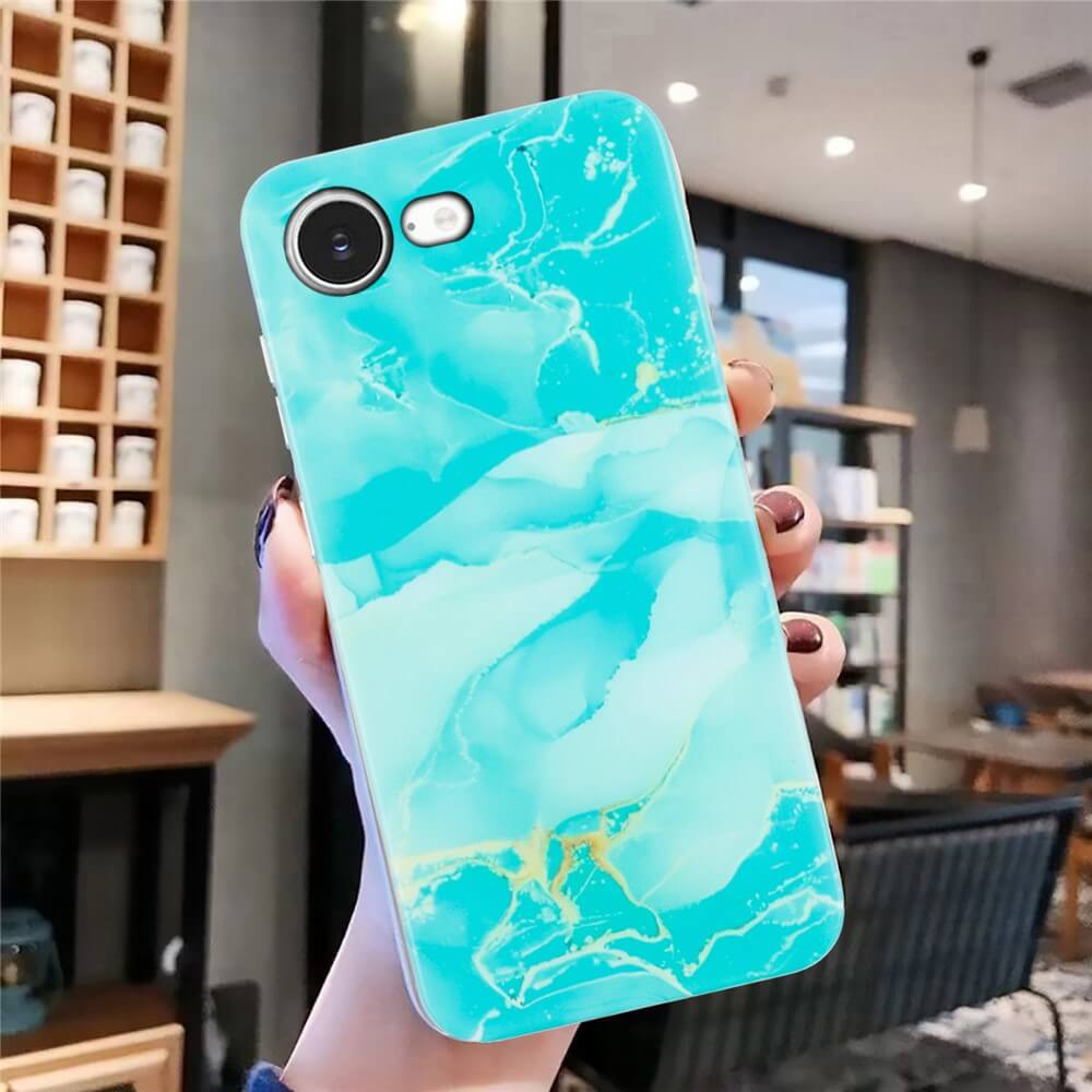 Eine Hand hält ein iPhone 16e in der Cover-Discount Silikon Hülle mit Marmor Motiv (türkis-gold) im modernen Café - stilvoller Schutz für dein Handy.