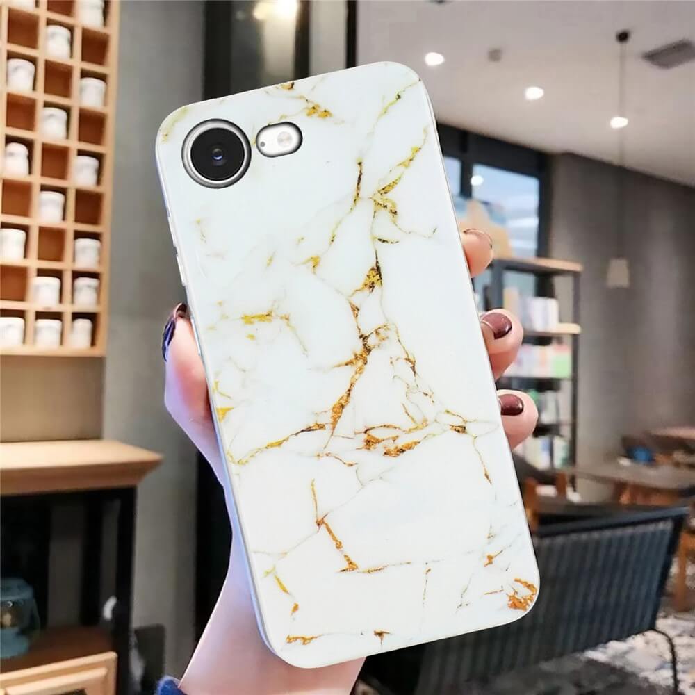 Eine Hand hält ein Telefon mit der Cover-Discount iPhone 16e - Silikon Hülle mit Marble Motiv in Weiß und Gold, ausgestellt in einem stilvollen, modernen Raum.