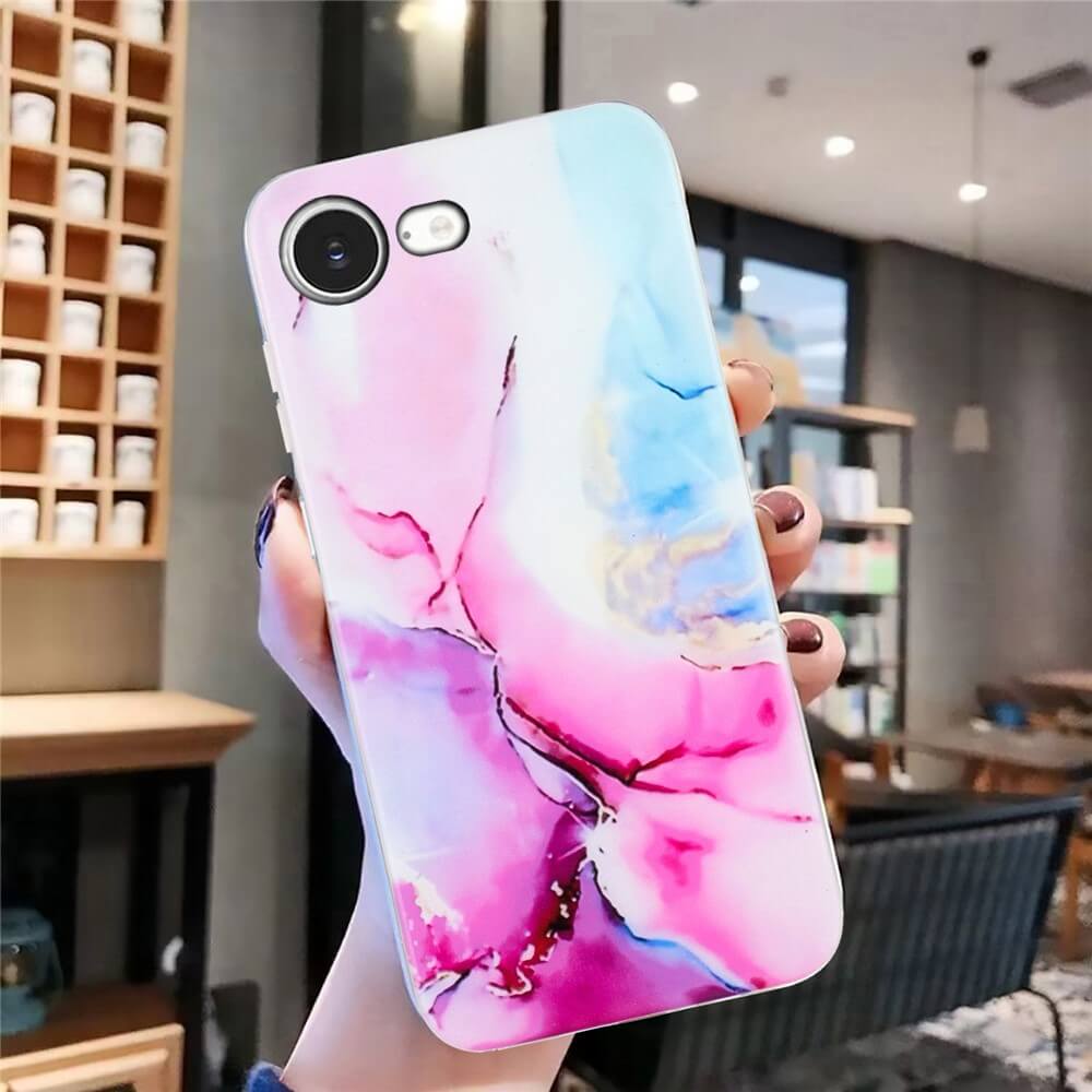 Eine Hand hält die Cover-Discount iPhone 16e - Silikon Hülle mit Marble Motiv (rosa und blau), eine stilvolle Handyhülle Schutz, in einem gemütlichen modernen Raum.