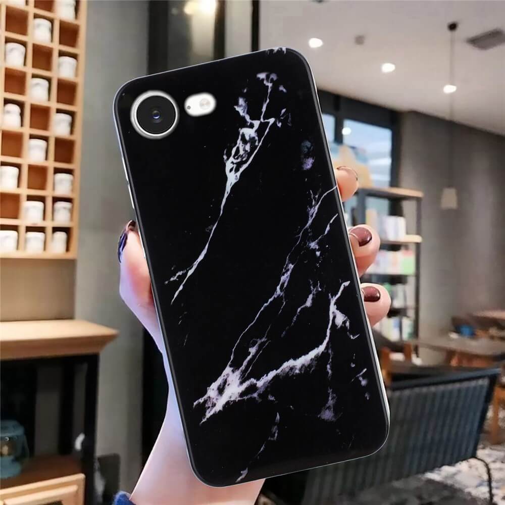Eine Hand hält ein Telefon mit der Cover-Discount iPhone 16e - Silikon Hülle mit Marble Motiv in Schwarz, dargestellt in einem modernen, gut beleuchteten Café.