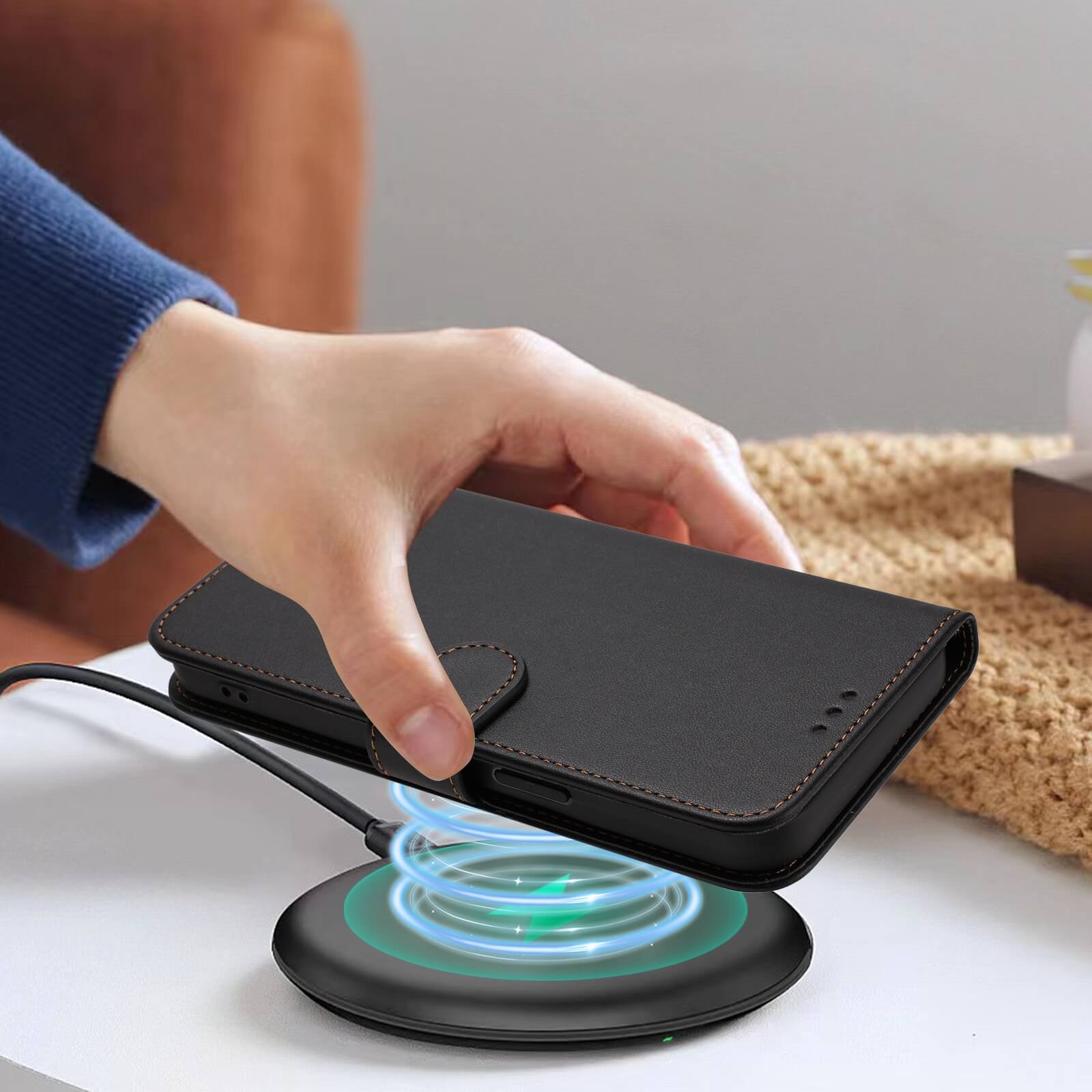 Eine Hand legt ein Cover-Discount iPhone 17 Pro Max Glänzendes Hüllen Etui mit Handschlaufe in Schwarz auf ein drahtloses Ladepad auf einem Tisch.