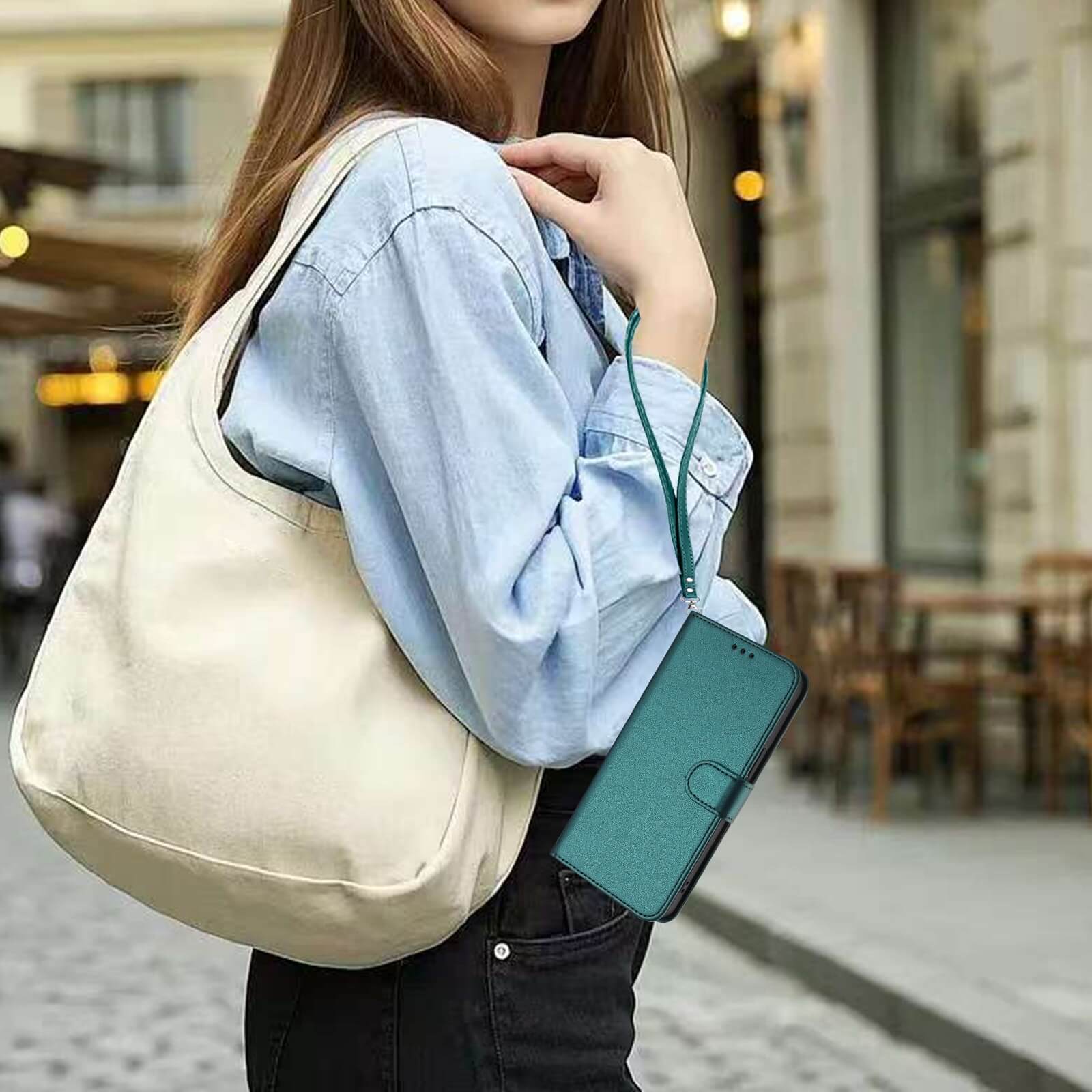 Eine Frau mit beiger Tasche und blauem Hemd hält das Cover-Discount iPhone 17 Pro Max - Glänzendes Hüllen Etui mit Handschlaufe im Freien auf einer Stadtstraße.