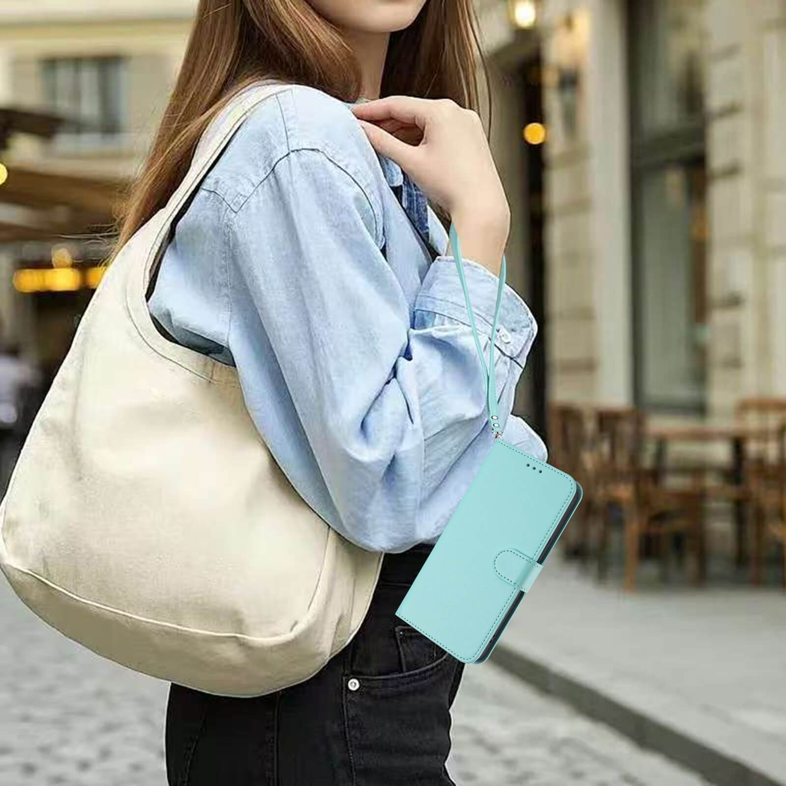 Frau im Jeanshemd trägt eine beige Tasche und hält ein Cover-Discount iPhone 17 Pro Max Glänzendes Hüllen Etui mit Handschlaufe im Freien.