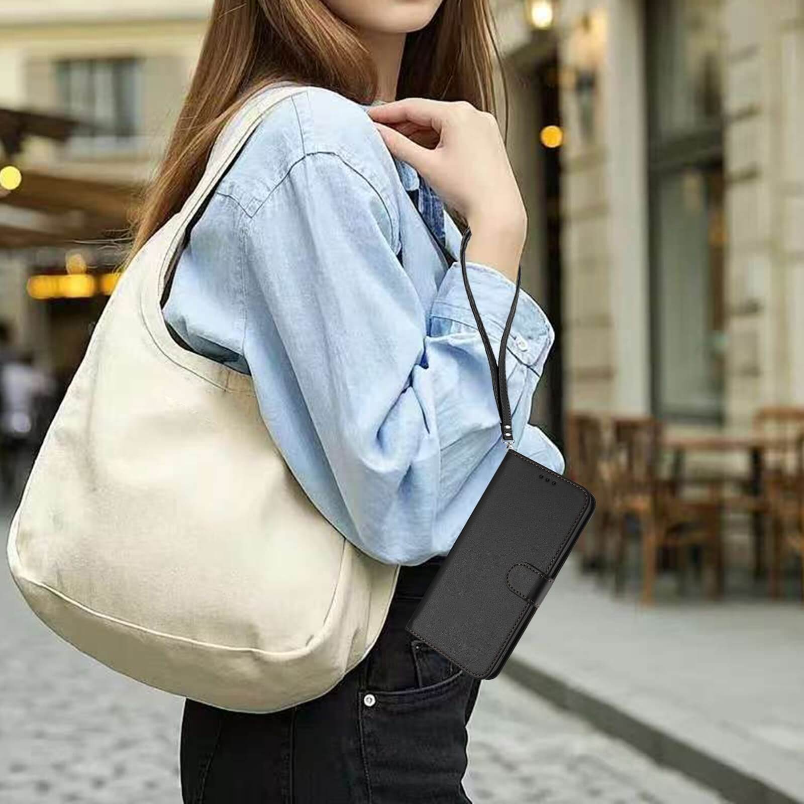 Eine Frau in einem hellblauen Hemd trägt eine cremefarbene Tasche und hält das Cover-Discount iPhone 17 Pro - Glänzendes Hüllen Etui mit Handschlaufe in der Hand, während sie durch die Stadt läuft.