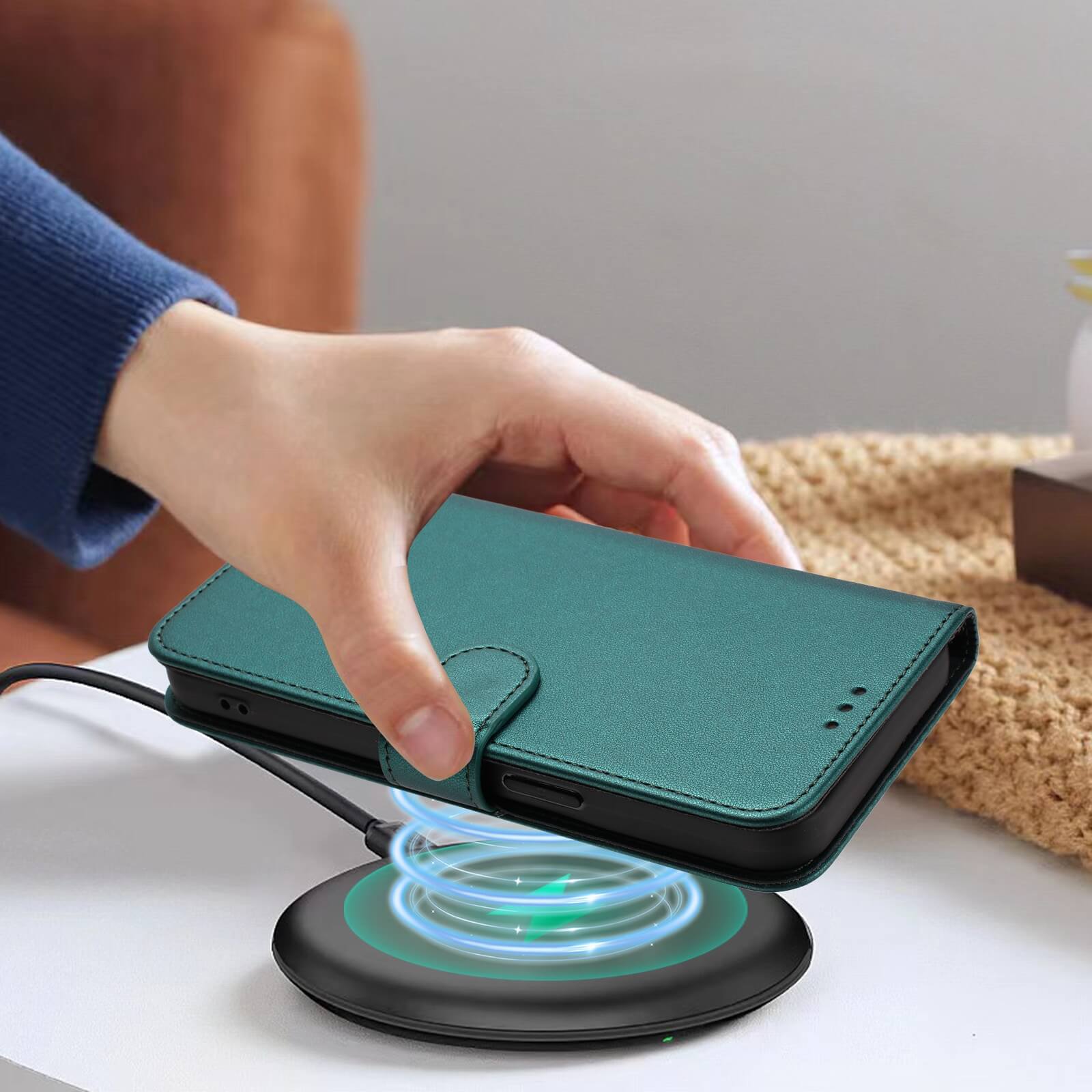 Eine Hand legt ein Cover-Discount iPhone 17 Pro - Glänzendes Hüllen Etui mit Handschlaufe in Teal auf ein drahtloses Ladepad auf einem Tisch.