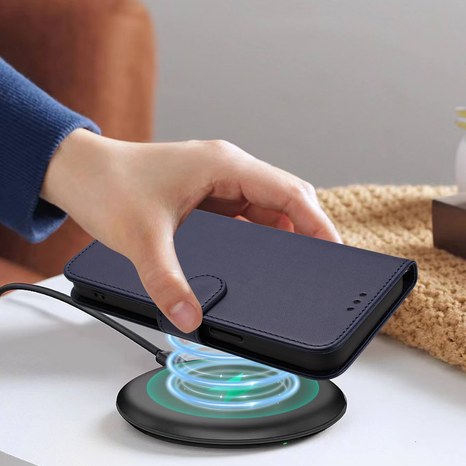 Eine Hand legt ein Cover-Discount iPhone 17 Pro - Glänzendes Hüllen Etui mit Handschlaufe in Navy auf ein Wireless Charging Pad auf einem weißen Tisch.