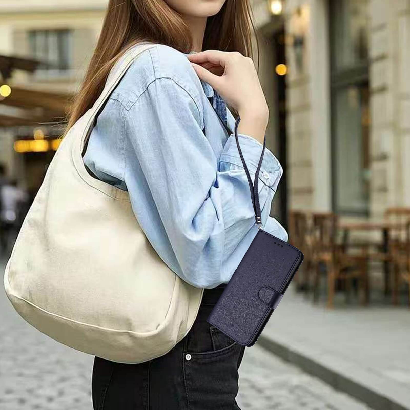 Eine Frau im hellblauen Hemd hält eine beigefarbene Tasche und ein schwarzes Portemonnaie und präsentiert das Cover-Discount iPhone 17 Pro Glänzendes Hüllen Etui mit Handschlaufe auf einer Straße in der Stadt.