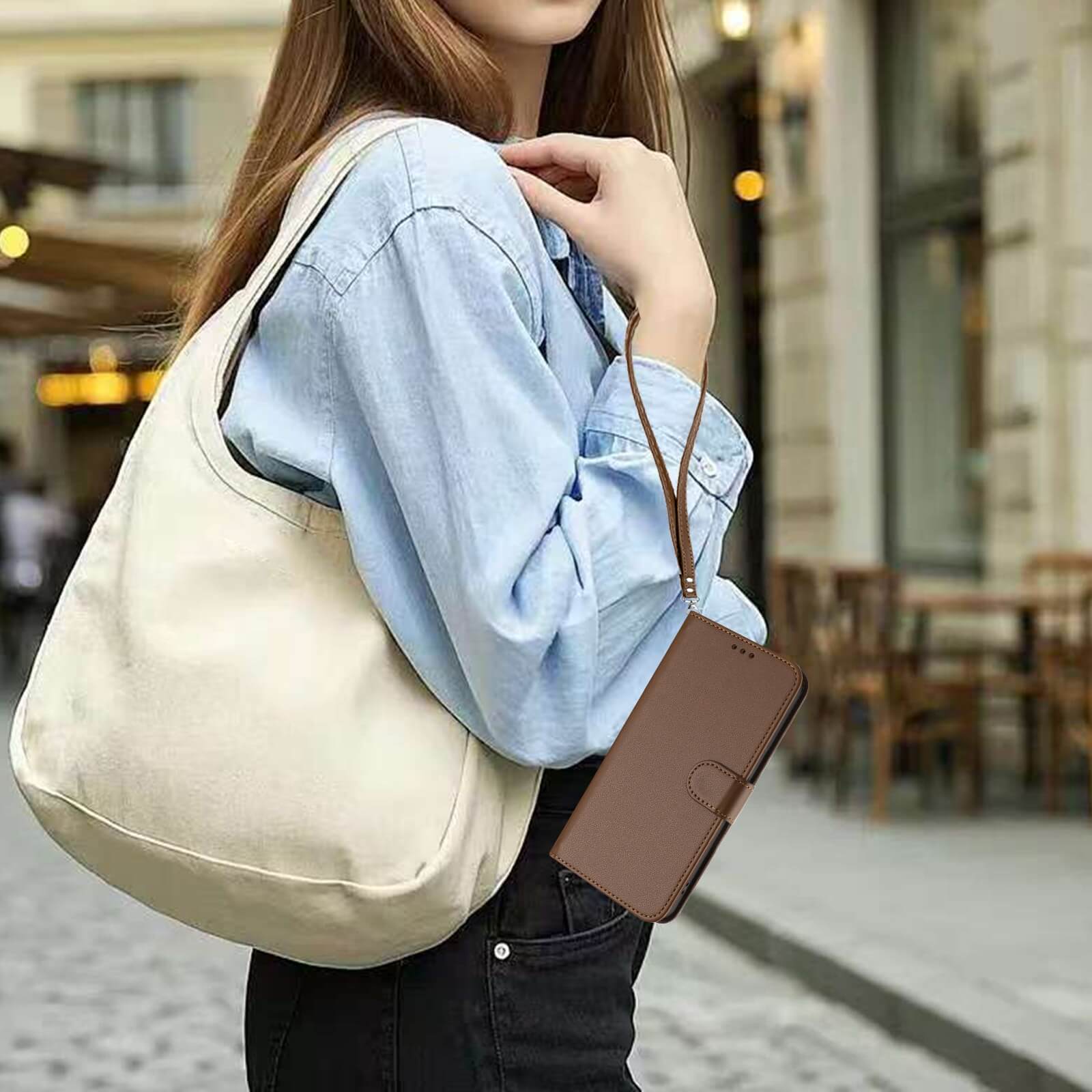 Frau in Jeanshemd und schwarzer Hose, die eine cremefarbene Umhängetasche trägt, in der sie das Cover-Discount iPhone 17 Air - Glänzendes Hüllen Etui mit Handschlaufe zusammen mit ihrem Handy Portemonnaie hält.