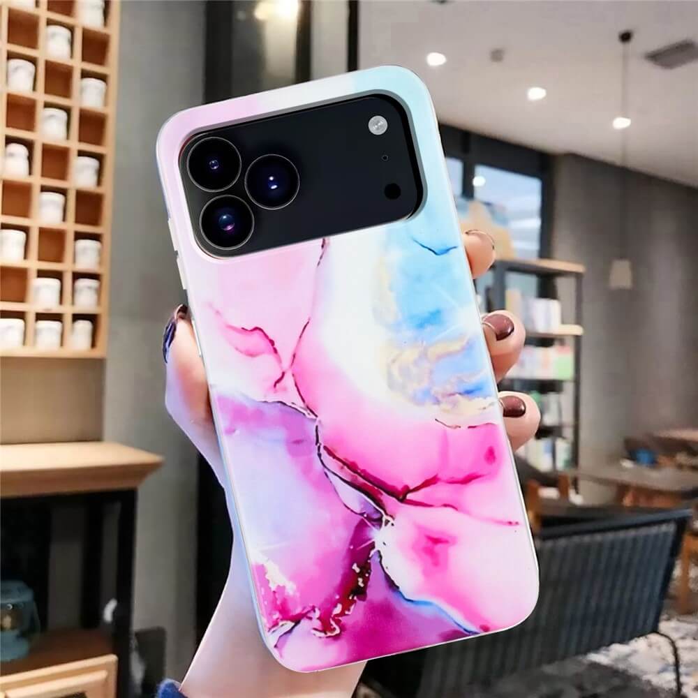 Eine Hand hält das Cover-Discount iPhone 17 Pro - Silikon Hülle mit Marble Motiv in Pink und Blau, ausgestellt in einem modernen Café.