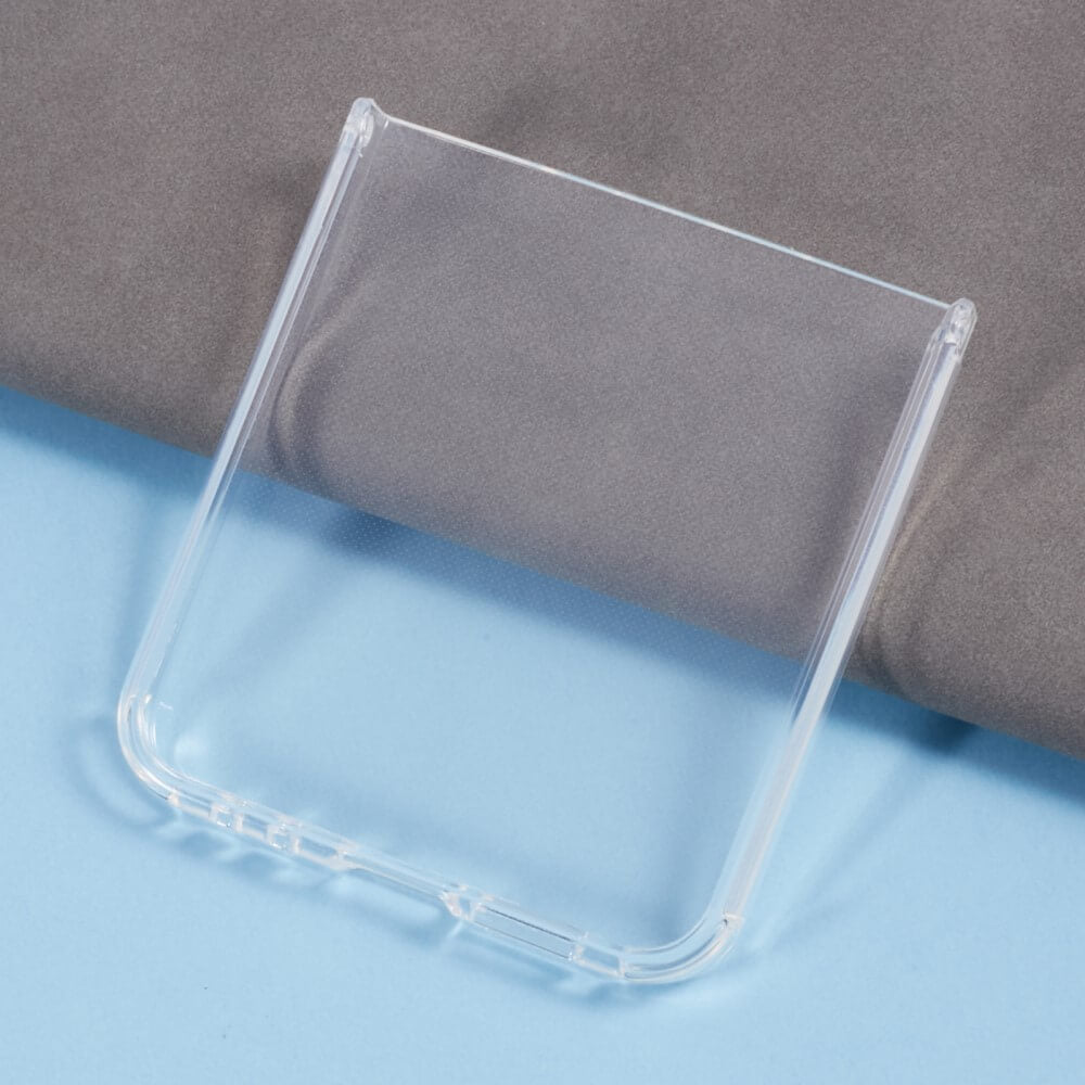 Das Cover-Discount Galaxy Z Flip6 - Silikon Gummi Case transparent liegt auf einer hellblauen Oberfläche, im Hintergrund ist teilweise ein grauer Stoff zu sehen.