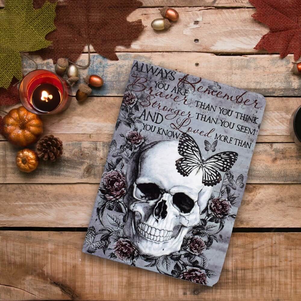 Ein Cover-Discount Kindle Paperwhite 2024 Etui mit stilvollem Motiv zeigt ein Design mit Schädel, Rosen und Schmetterling und bietet einzigartigen Stil sowie Rundumschutz - perfekt präsentiert auf einem rustikalen Holztisch mit Herbstdeko und Kerzen.