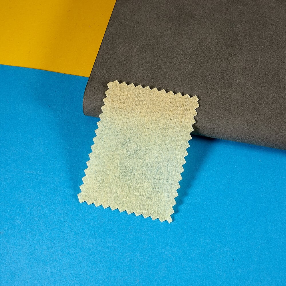 Ein rechteckiges beiges Tuch mit Zickzack-Kanten liegt auf blauem, gelbem und dunkelgrauem Hintergrund – ideal zum Reinigen Ihres Cover-Discount Galaxy A16 – Display-Schutzfolie PET oder anderer ultradünner Displayschutzfolien.