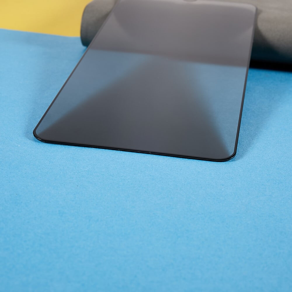 Das Galaxy A16 – Panzerglas Display Privacy Anti-Spy von Cover-Discount mit dunklem Bildschirm liegt auf einer blauen Oberfläche neben einer aufgerollten grauen Matte, alles vor einem gelben Hintergrund.
