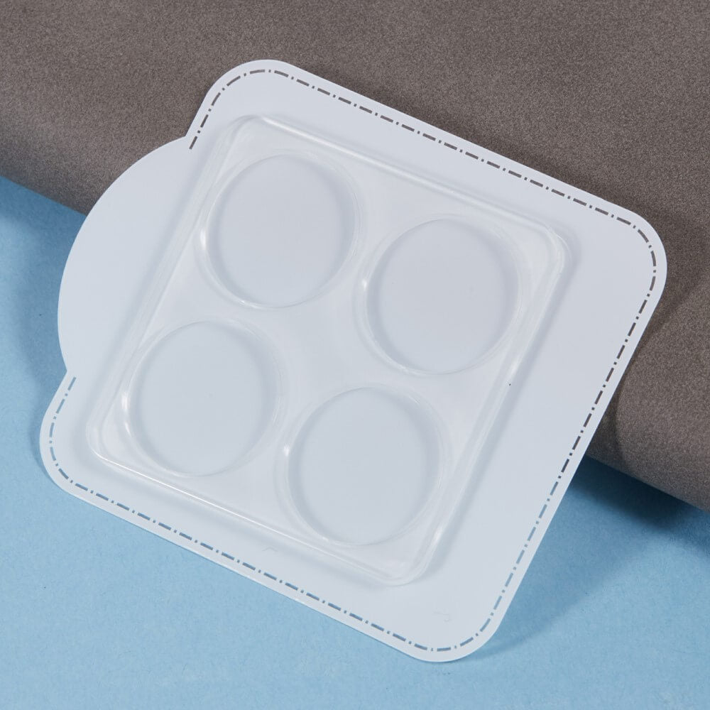 Eine weiße Plastikblisterpackung mit vier leeren ovalen Schlitzen für Cover-Discount Xiaomi 14T Pro – 2 Stk. Panzerglas Kamera liegt auf einer blau-grauen Oberfläche.