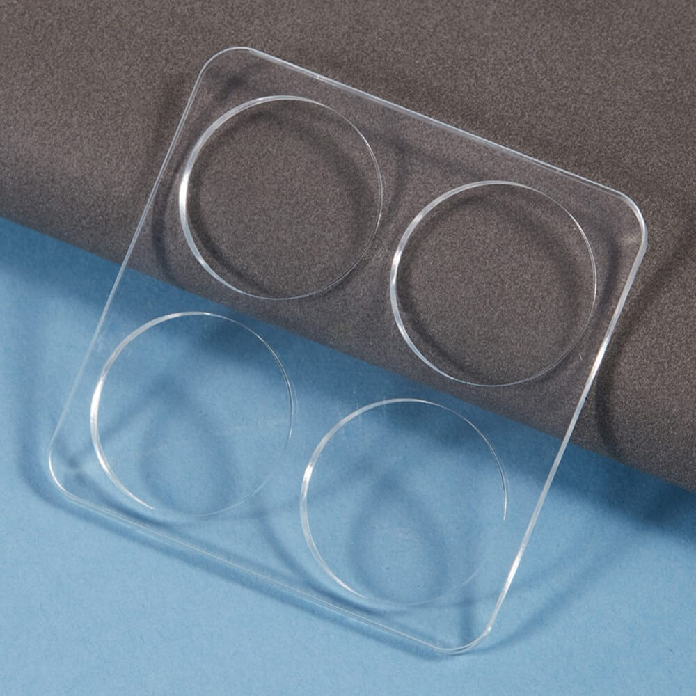 Eine durchsichtige quadratische Kunststoffform mit vier kreisförmigen Vertiefungen, perfekt zum Formen von gehärtetem Glas für das Cover-Discount Xiaomi 14T Pro – 2 Stk. Panzerglas Kamera, abgebildet auf einem blau-grauen Hintergrund.