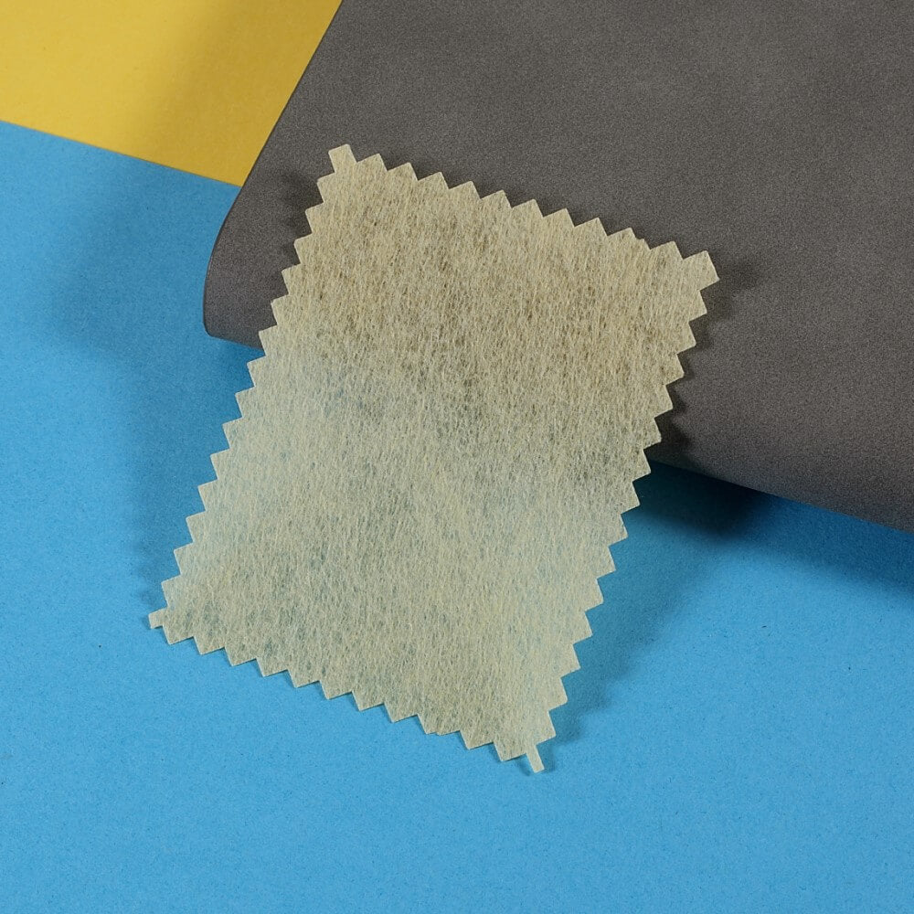 Ein strukturierter rechteckiger Stoff mit Zickzack-Kanten liegt auf blauem, gelbem und grauem Papier und ähnelt dem Schichtstil der Cover-Discount Galaxy S25 / S24 Display-Schutzfolie PET Privacy Anti-Spy.