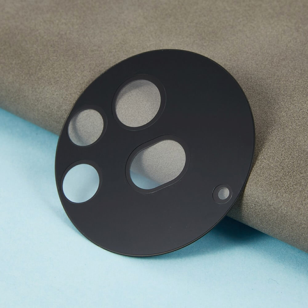 Cover-Discount Nothing Phone (3a) Pro - 2 Stk. Panzerglas Kamera: Schwarze, runde Linsenschutzabdeckung mit mehreren Aussparungen für optimalen Schutz, auf hellblau-grauem Untergrund.