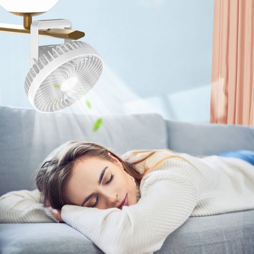 Eine Frau schläft auf einer Couch unter einem kompakten weißen Mini-Ventilator Camping tragbar von Cover-Discount, der über ihr angebracht ist, während das Sonnenlicht hereinströmt.
