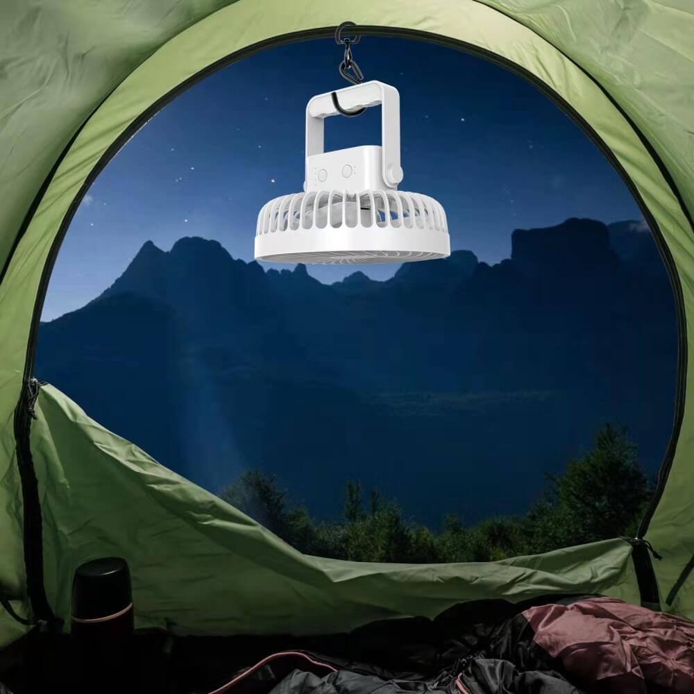 Eine Laterne hängt in einem Zelt, durch dessen offene Tür Berge und ein sternenklarer Nachthimmel sichtbar sind, während ein tragbarer Mini-Ventilator von Cover-Discount für frische Luft im Zelt sorgt.