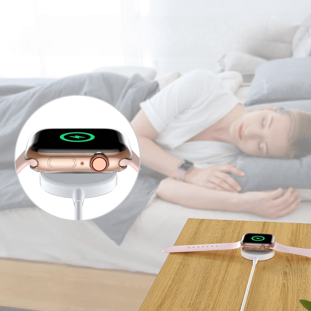 Eine Apple Watch 10 â 46 mm mit einem transparenten Gummi-Schutzgehäuse von Cover-Discount wird auf einem Nachttisch aufgeladen, während im Hintergrund eine Frau friedlich schläft.