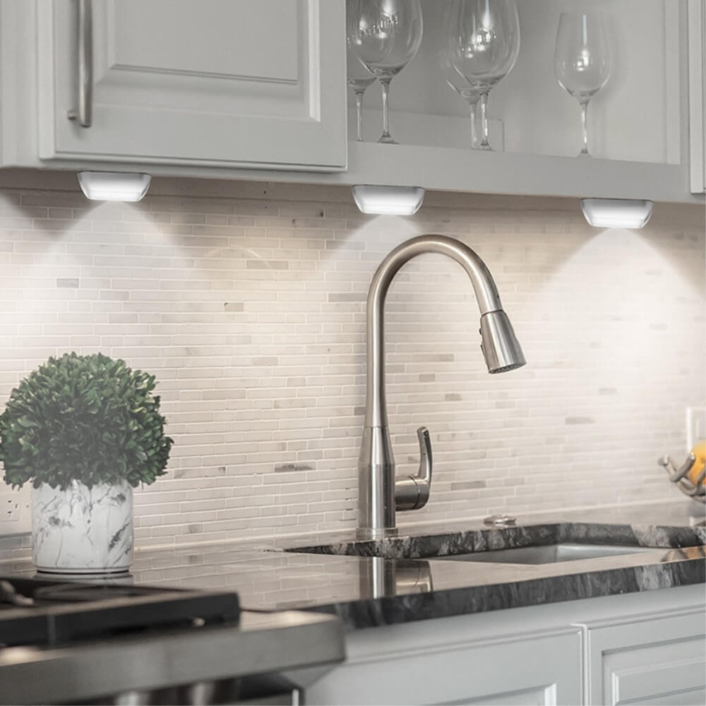 Moderne Küche mit Cover-Discount 3er Set LED Licht mit Sensor Triangle – batteriebetrieben, unter dem Schrank, Bewegungs-Sensor und einfache, kabellose Anbringung mit Klebepunkten – dazu ein stylisches Spülbecken und Pflanze auf schwarzer Arbeitsfläche.