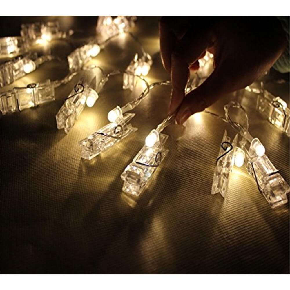 Eine Hand berührt die Cover-Discount Lichterkette LED Fotoklammer, batteriebetrieben, während ihre leuchtenden Clips auf einer strukturierten Oberfläche warm funkeln und eine gemütliche Atmosphäre schaffen.