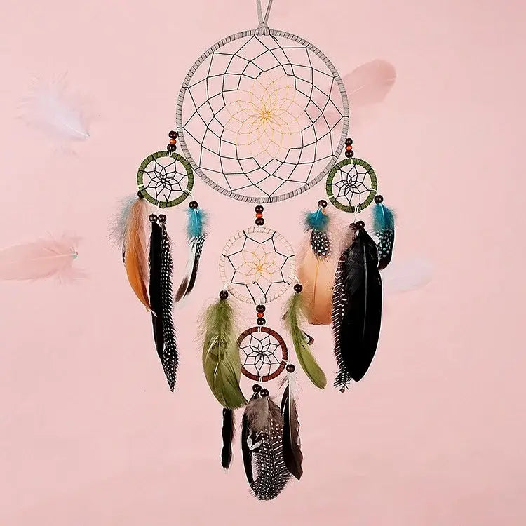 Der stilvolle Traumfänger mit 5 Ringen in Naturtönen von Cover-Discount mit Federn und Perlen hängt vor sanftem Rosa und ist ein bezauberndes Dekorationsstück.