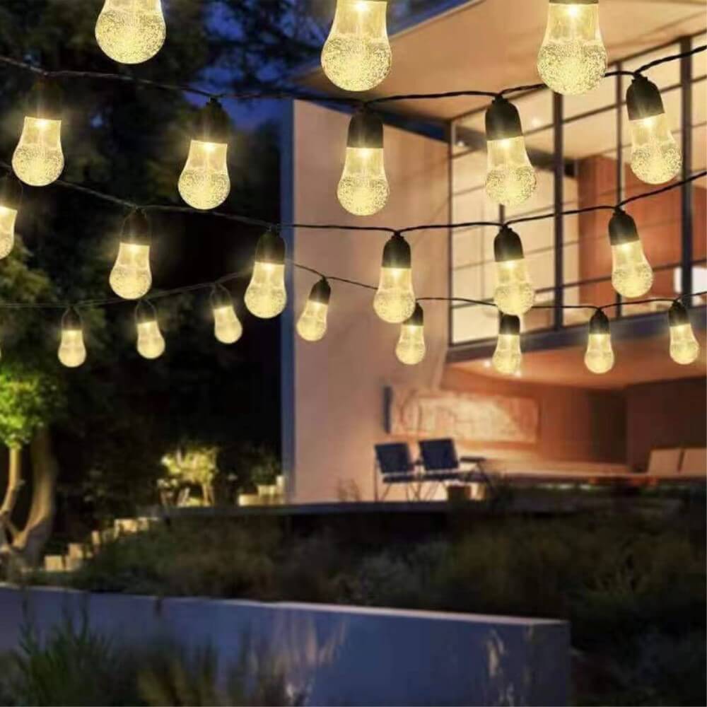 Cover-Discount Solar LED Lichterkette Glühbirnen hängen an einem modernen Haus bei Dämmerung, beleuchten die Terrasse und sorgen für stimmungsvolle Gartenbeleuchtung.