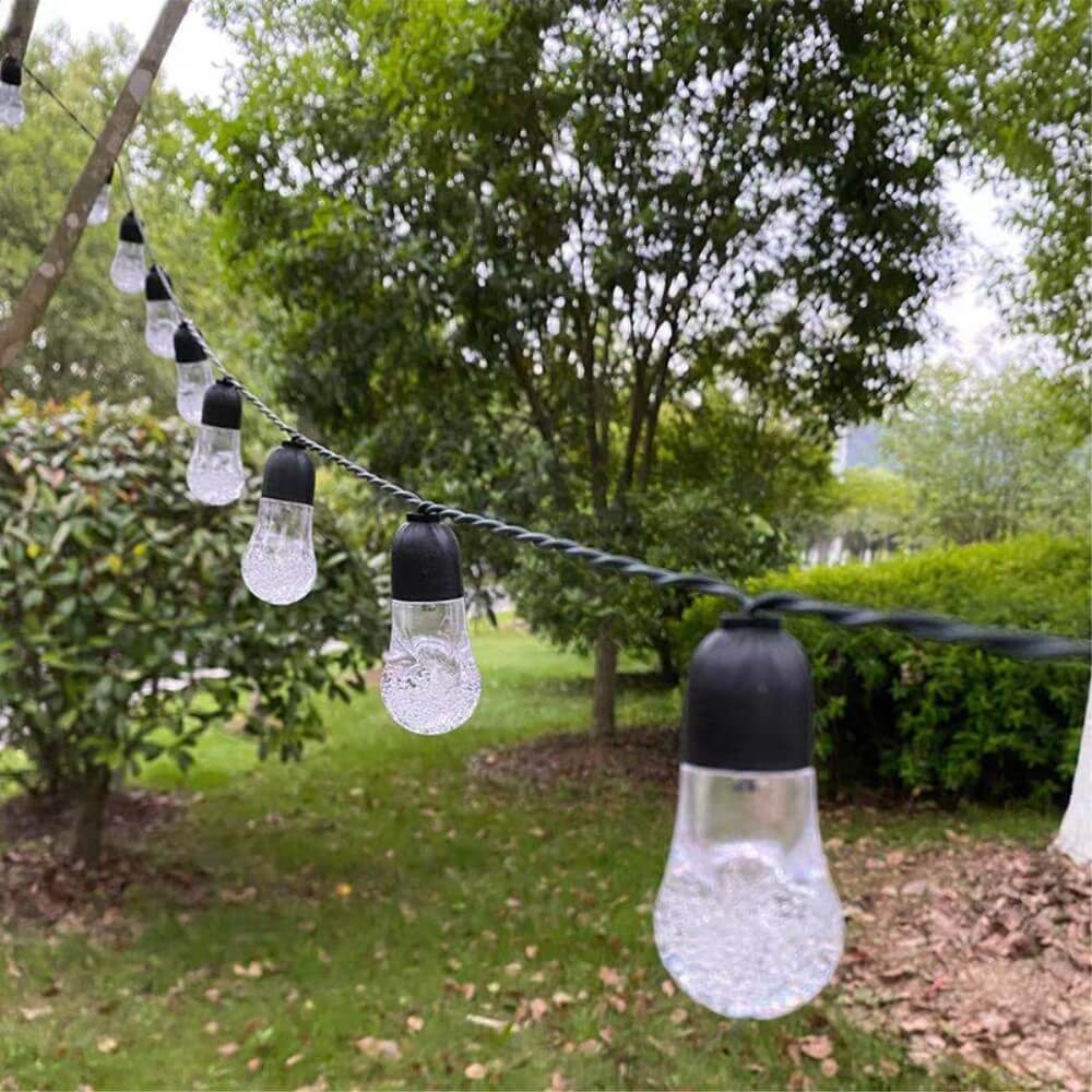 Die Solar LED Lichterkette Glühbirnen von Cover-Discount erzeugen warmes Licht und sorgen für stimmungsvolle Gartenbeleuchtung zwischen Bäumen und im Gras.