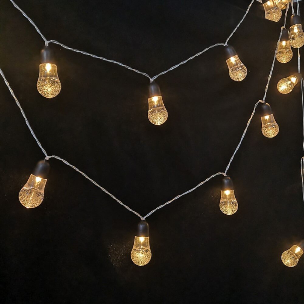 Die Solar LED Lichterkette Glühbirnen von Cover-Discount sorgen mit warmem LED-Licht für stimmungsvolle Beleuchtung im Garten – leuchtende Glühbirnen als dekorativer Blickfang vor dunklem Hintergrund.