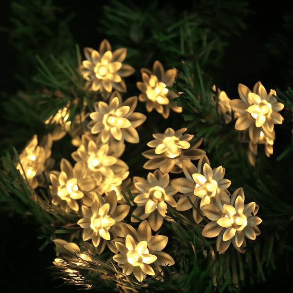 Die Solar LED Lichterkette Lotusblüte von Cover-Discount verleiht grünen Tannenzweigen im Garten als stilvolle Beleuchtung ein stimmungsvolles Ambiente im Dunkeln.