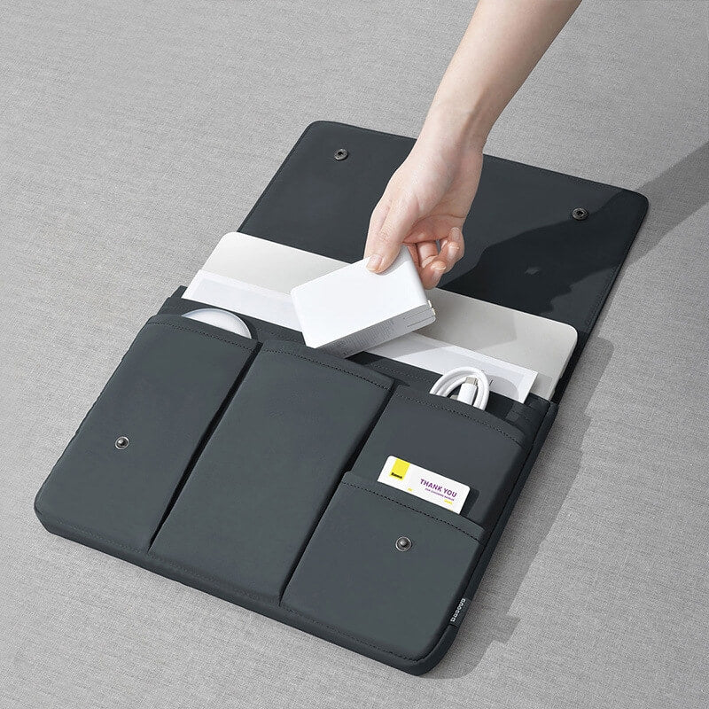 Eine Hand legt eine externe Festplatte in die Cover-Discount Laptop-Hülle Tasche für Notebook, eine schwarze Hülle mit organisierten Fächern, auf einer grauen Oberfläche.