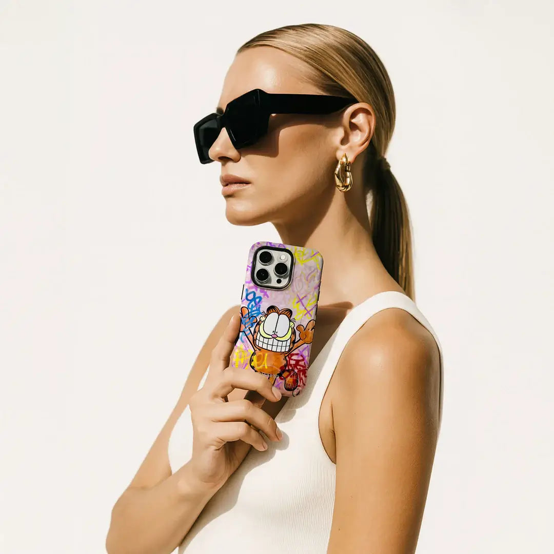 Frau mit Sonnenbrille und goldenen Ohrringen hält die Casarto iPhone 17 Pro Handyhülle Happy Day-MagSafe kompatibel, Limited Art Edition, die perfekt zu ihrem weißen Oberteil passt.