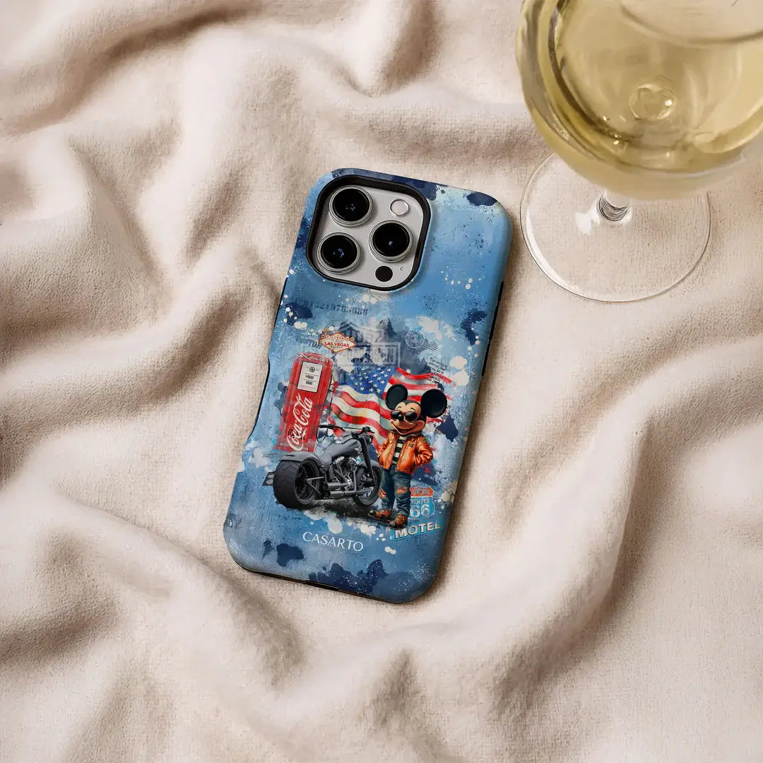 Eine blaue Cover-Discount Casarto "Ride the dream" iPhone 17 Pro Hülle mit einem Collage-Design, Limited Edition und MagSafe kompatibel, sitzt neben einem Glas Weißwein auf beigem Stoff.