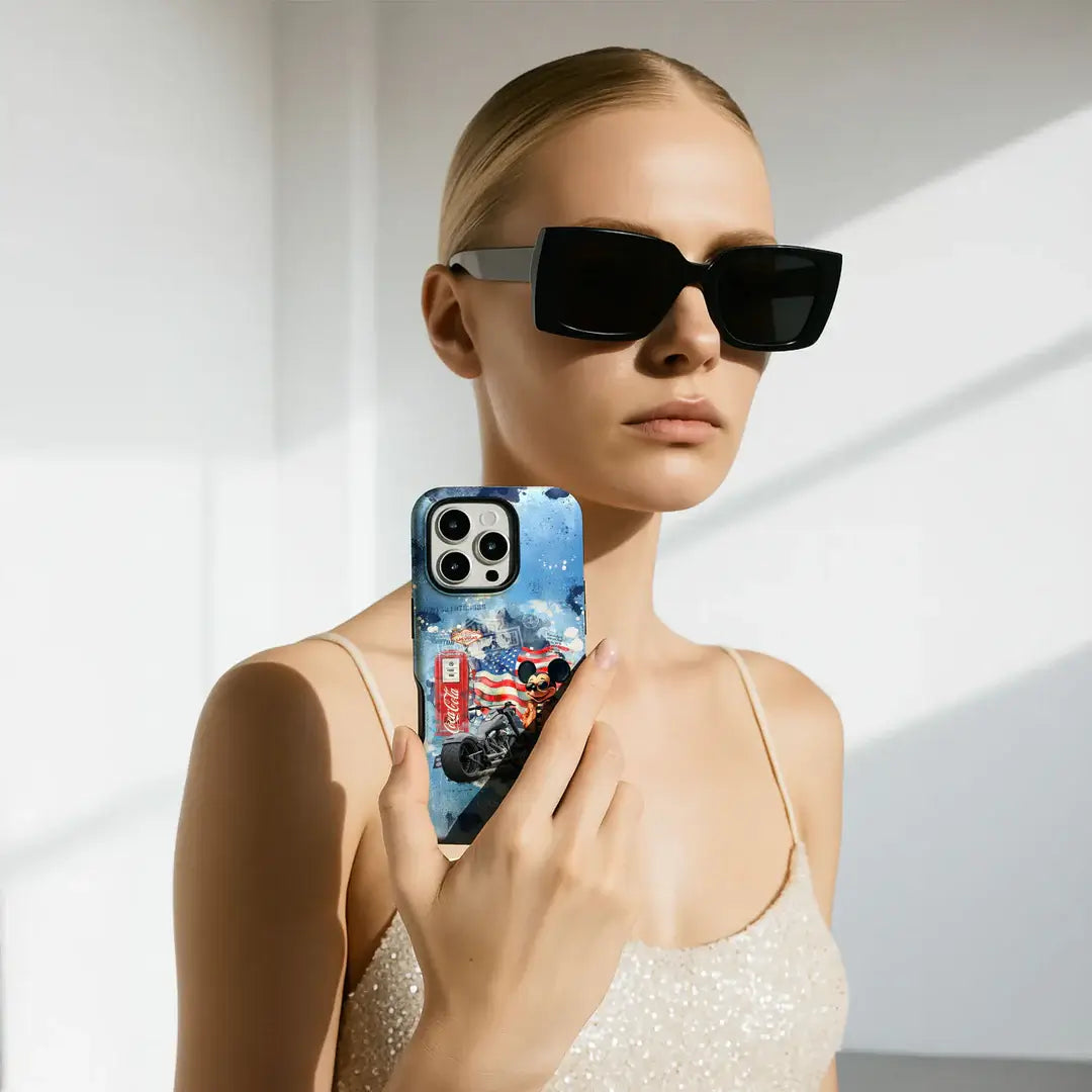 Eine Frau mit Sonnenbrille hält ihr Handy mit der limitierten Cover-Discount Casarto Handyhülle "Ride the dream" für iPhone 17 Pro, MagSafe kompatibel, gepaart mit einem glitzernden beigen Camisole für müheloses Aufladen und lebendigen Marvel-inspirierten Stil.