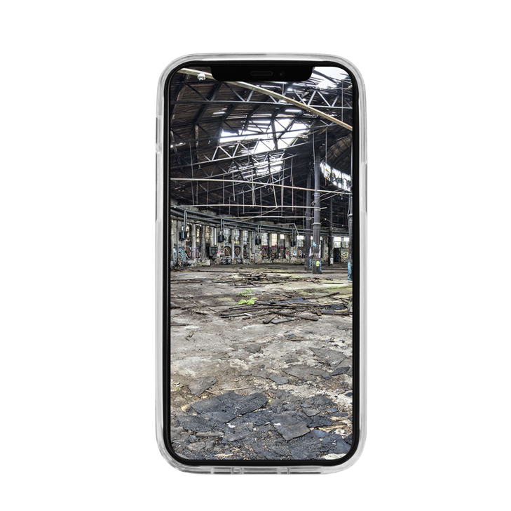 Ein JT Berlin iPhone 13 mini / 12 mini in einem Pankow Clear Case macht ein Foto von einem verlassenen, heruntergekommenen Industriegebäude mit einem beschädigten Dach.