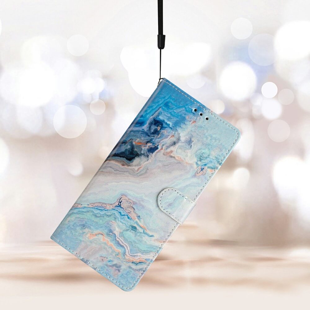 Die blau-weisse Hülle mit Marmormuster für das Galaxy A36 5G – Discount – Tasche mit Motiv, die an einem schwarzen Riemen mit unscharfem Hintergrund hängt, bietet Rundum-Schutz.