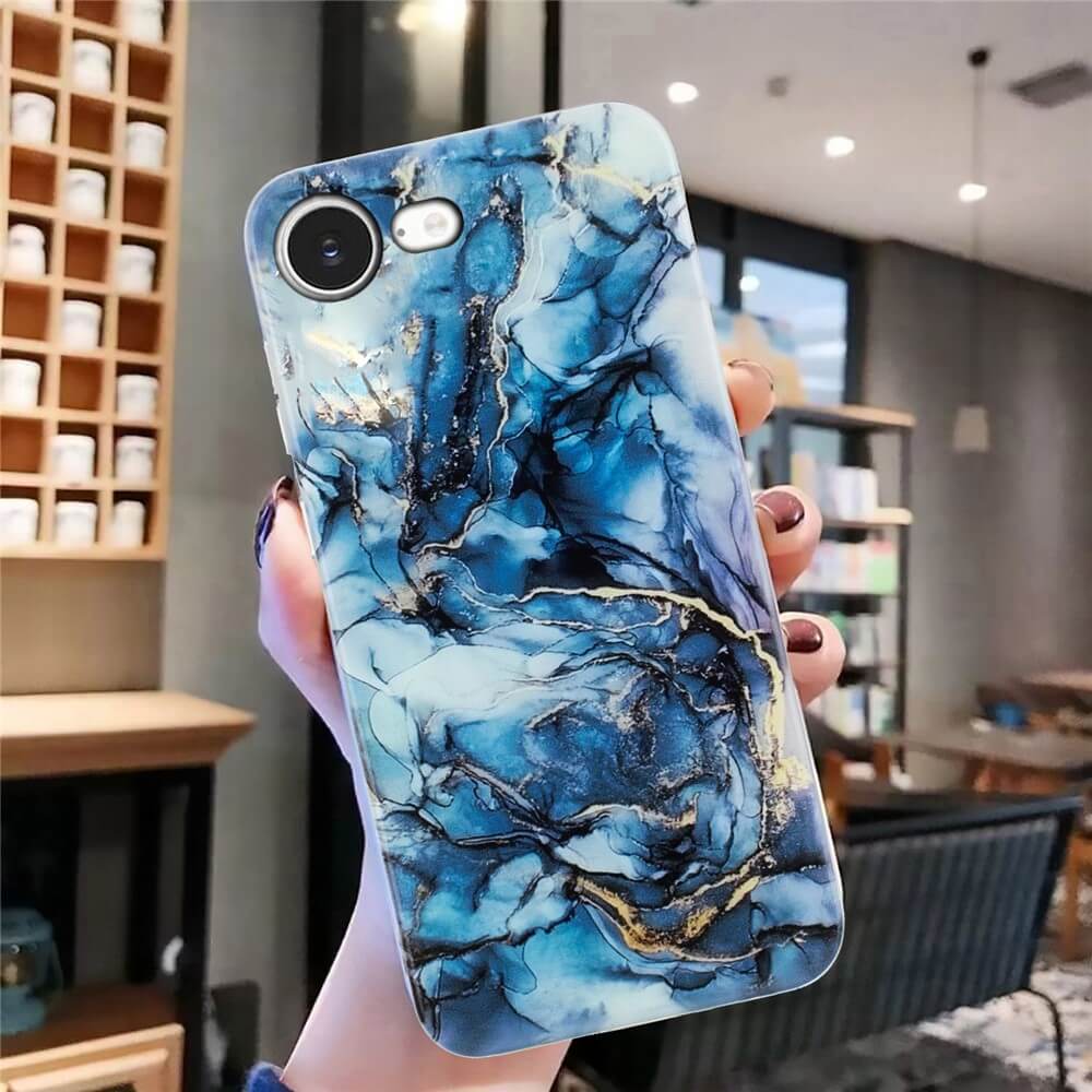 Eine Hand hält das Cover-Discount iPhone 16e - Silikon Hülle mit Marble Motiv in Blau und Gold, ausgestellt in einem modernen, gut beleuchteten Raum.