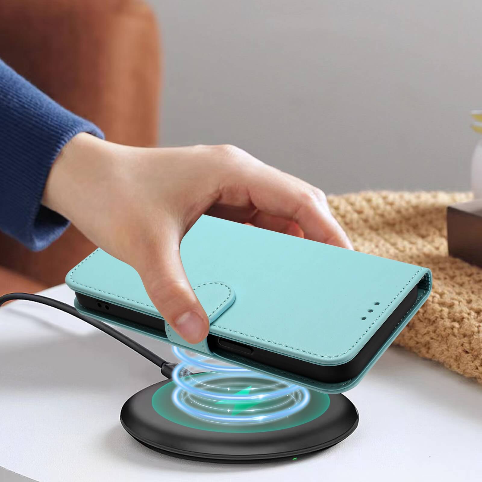 Eine Hand legt das Cover-Discount iPhone 17 Air - Glänzendes Hüllen Etui mit Handschlaufe in Blau auf ein drahtloses Ladepad auf einem weißen Tisch.