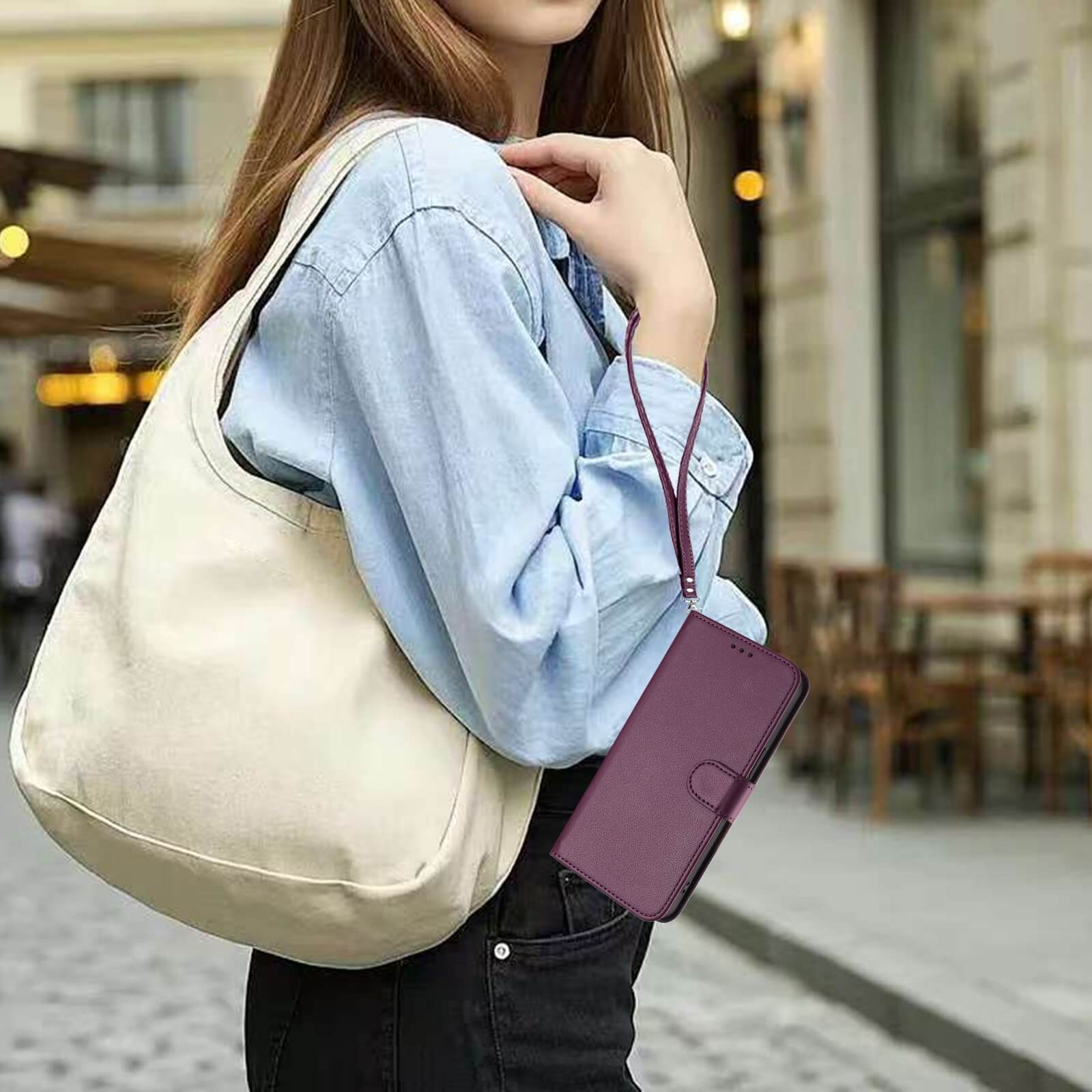Eine Frau in einem blauen Hemd mit einer weißen Tasche hält das Cover-Discount iPhone 17 - Glänzendes Hüllen Etui mit Handschlaufe auf einer Straße in der Stadt.