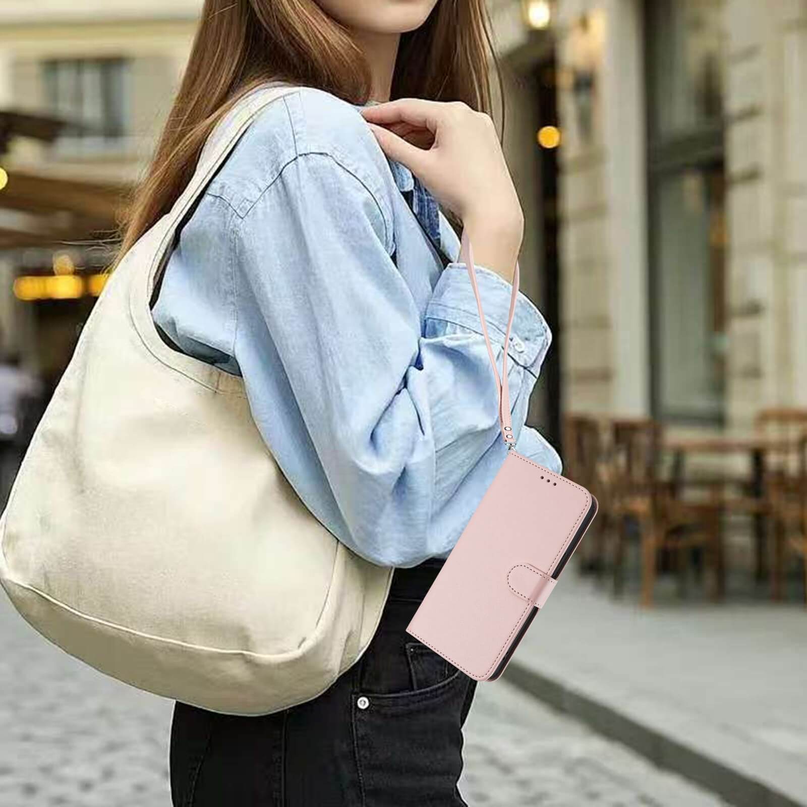 Eine Frau mit einer cremefarbenen Tragetasche hält das pinkfarbene iPhone 17 - Glänzendes Hüllen Etui mit Handschlaufe von Cover-Discount in der Hand und kombiniert es mit ihrem hellblauen Hemd zu einem schicken Look.