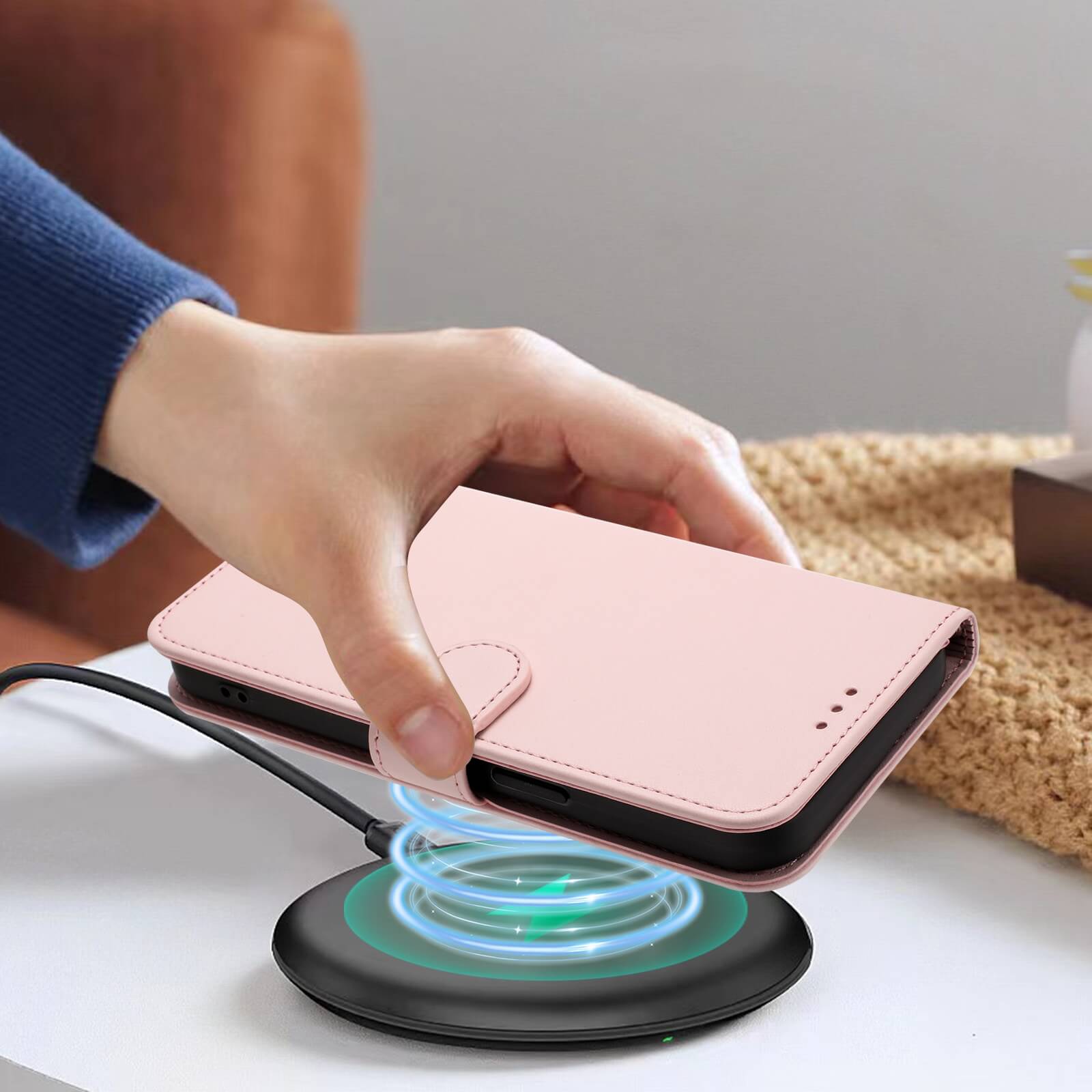Eine Hand legt ein rosa Cover-Discount iPhone 17 - Glänzendes Hüllen Etui mit Handschlaufe auf ein schwarzes kabelloses Ladepad, das auf dem Tisch liegt.