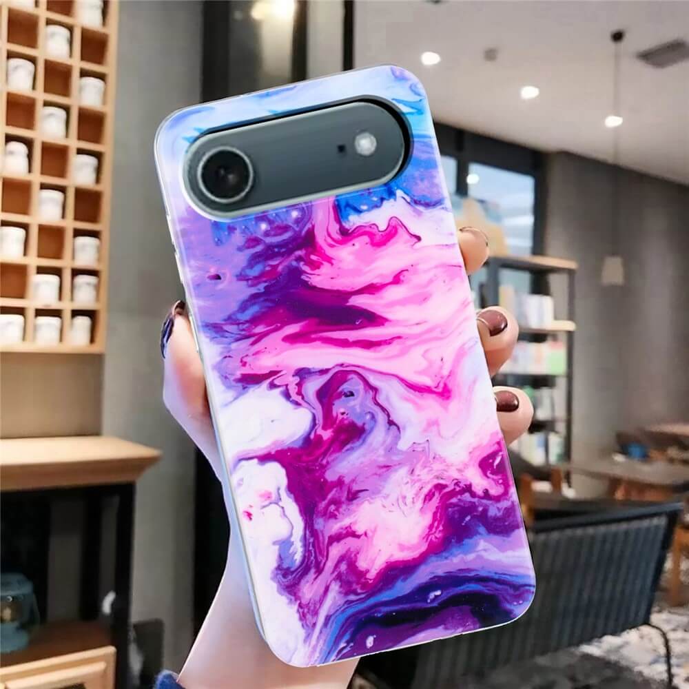 Eine Hand hält die Cover-Discount iPhone 17 Air - Silikon Hülle mit Marble Motiv in rosa, lila und weißem Marmordesign in einem modernen Café.