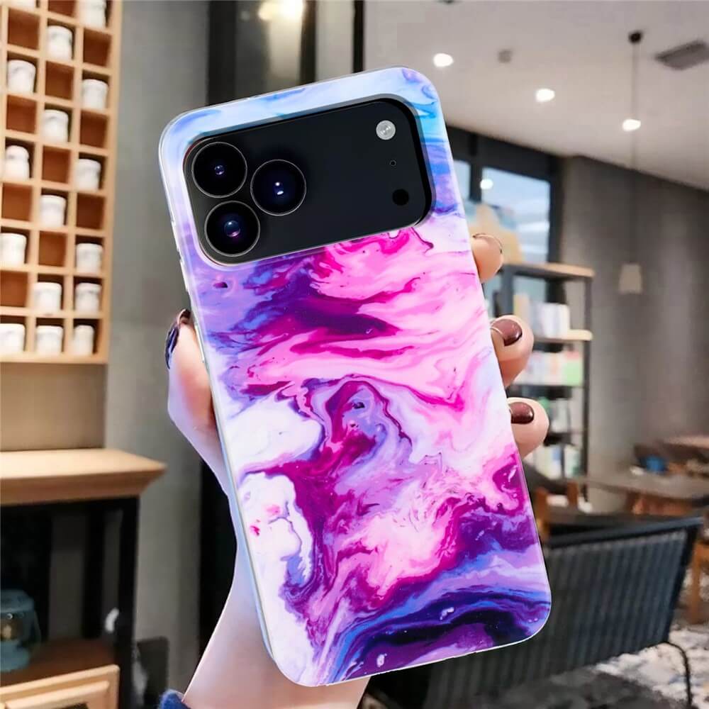Eine Hand hält die Cover-Discount iPhone 17 Pro Max - Silikon Hülle mit Marble Motiv in Pink, Lila und Weiß und setzt damit ein stilvolles Statement in einem modernen Café.