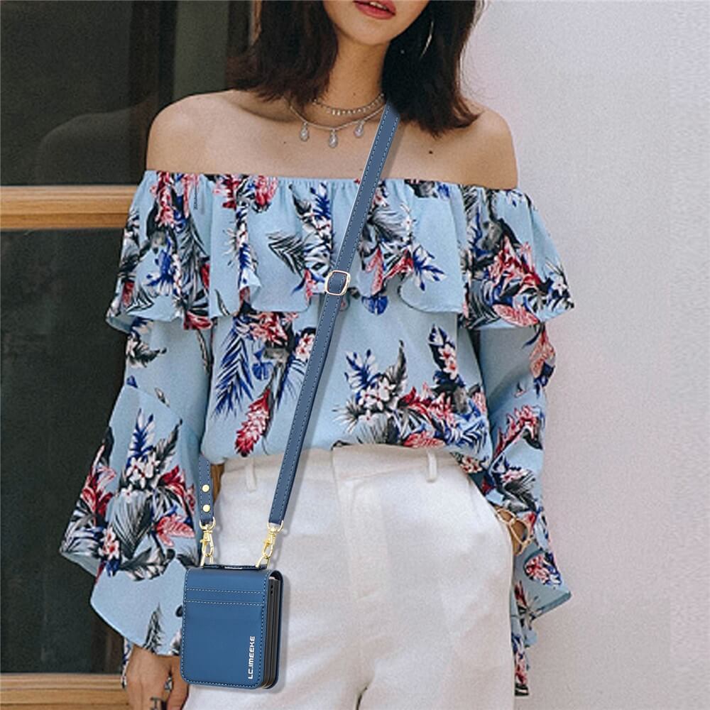 Eine Frau in blauer, geblümter Off-Shoulder-Bluse, weißer Hose und blauer Crossbody-Handtasche steht an einem Fenster und trägt ihr Galaxy Z Flip7 in der LC.IMEEKE L1 Series Leder Etui Hülle, die ihren eleganten Stil perfekt ergänzt.