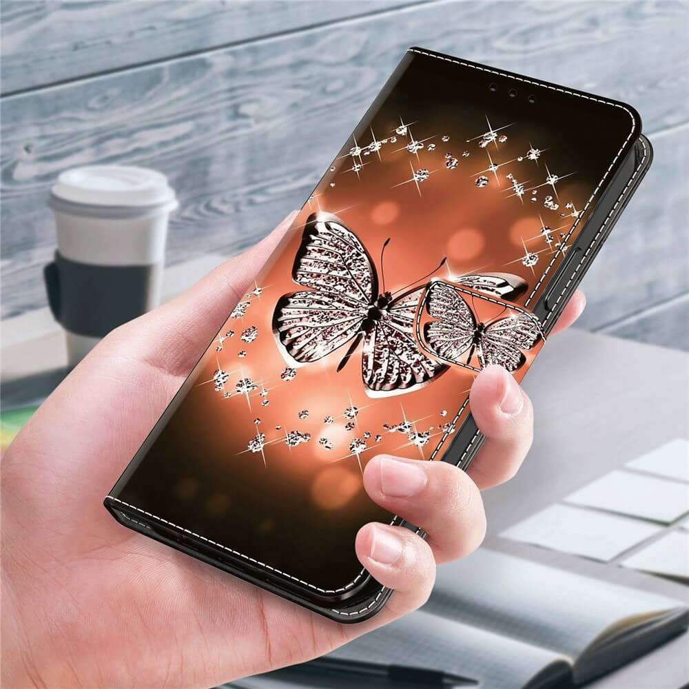Eine Hand hält ein Galaxy A35 mit dem Cover-Discount 3D-Effekt Hülle Etui mit glitzerndem Schmetterlingsdesign vor einem unscharfen Hintergrund aus Kaffeetasse und Schreibtisch.