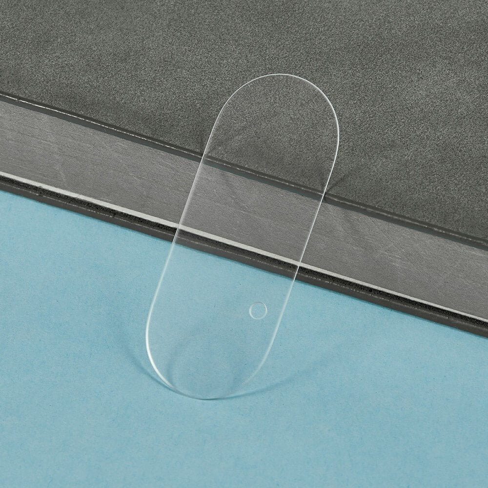 Transparenter, ovaler Gegenstand mit abgerundeten Kanten auf hellblauer Oberfläche vor grauem Hintergrund.