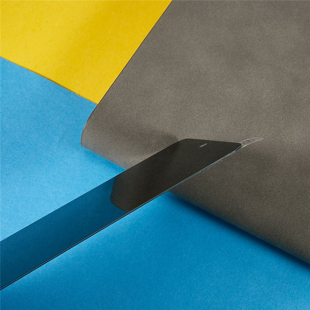 Ein Universalmesser schneidet graues Papier auf blauem und gelbem Grund und erinnert an die Präzision, die erforderlich ist, um die Cover-Discount Google Pixel 10 / 10 Pro - Panzerglas Display Privacy Anti-Spy Displayschutzfolie anzubringen.